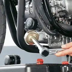 Motorrad-Ölfilter wird mit einem Werkzeug gewechselt, daneben ein neuer Filter und eine Ölauffangwanne.