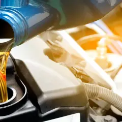 Frisches Öl wird aus einem blauen Behälter in einen Motor gegossen.