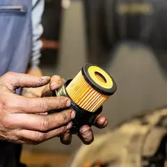 Hände halten einen neuen, gelben Ölfilter für ein Auto.