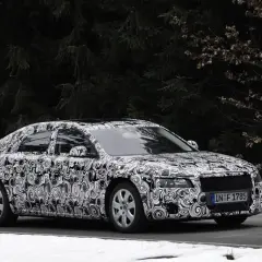 Audi Limousine mit Tarnfolie fährt auf schneebedeckter Straße vor dunklem Wald.
