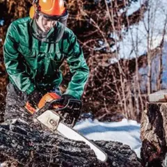 Mann in Schutzkleidung sägt mit Kettensäge in winterlicher Waldlandschaft.