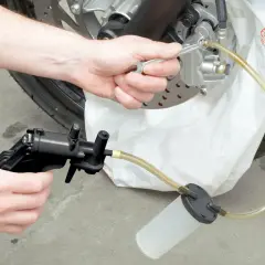 Hand wechselt Bremsflüssigkeit an Motorrad mit Werkzeug und Auffangbehälter.