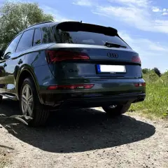 Dunkelgrüner Audi Q5 auf Schotterweg, im Hintergrund grüne Wiesen und Bäume.