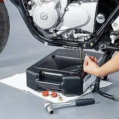 Motorrad-Ölwechsel: Hand leert Öl aus Motor in Auffangwanne. Werkzeug liegt bereit.