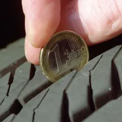 Daumen und 1-Euro-Münze messen Reifenprofiltiefe.