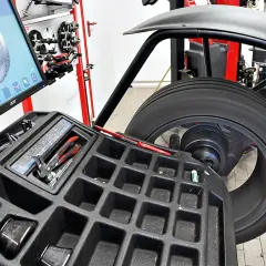 Reifen auf einer Wuchtmaschine mit Bildschirm und Werkzeugablage.