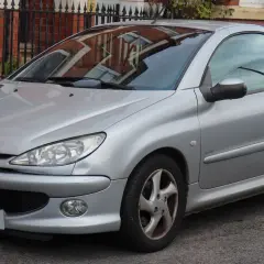 Silberner Peugeot 206 CC mit offenem Verdeck, geparkt vor einer Ziegelmauer.