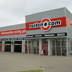 Fassade des reifen.com-Geschäfts mit roten Rolltoren und Reifenregalen im Fenster.