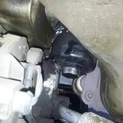 Schwarzer Ölfilter an einem Auto-Motor, umgeben von Metallteilen und Kabeln.