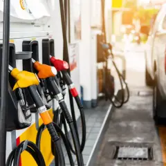 Zapfsäulen mit bunten Zapfpistolen und einem Teil eines Autos an einer Tankstelle.