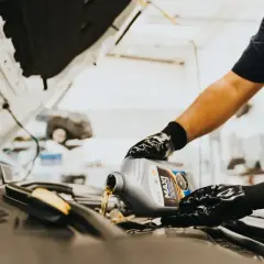 Person mit Handschuhen gießt Motoröl aus einem Kanister in einen Auto-Motor.