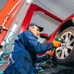 Mechaniker wechselt Reifen an einem roten Auto mit einem Schlagschrauber.