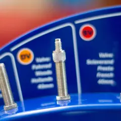 Drei Fahrradventile auf blauem Hintergrund mit Beschriftungen.