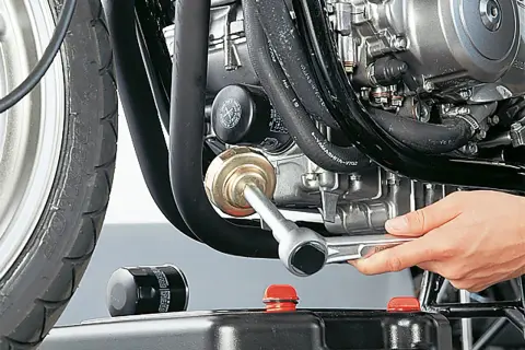 Motorrad-Ölfilter wird mit einem Werkzeug gewechselt, daneben ein neuer Filter und eine Ölauffangwanne.