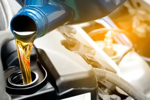 Frisches Öl wird aus einem blauen Behälter in einen Motor gegossen.