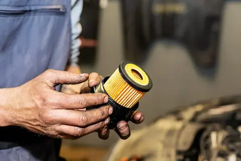 Hände halten einen neuen, gelben Ölfilter für ein Auto.