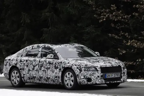 Audi Limousine mit Tarnfolie fährt auf schneebedeckter Straße vor dunklem Wald.