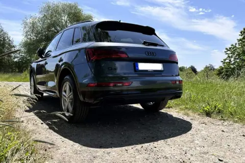 Dunkelgrüner Audi Q5 auf Schotterweg, im Hintergrund grüne Wiesen und Bäume.