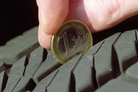Daumen und 1-Euro-Münze messen Reifenprofiltiefe.