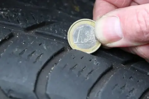 Nahaufnahme eines Reifens, auf dem eine 1-Euro-Münze zur Messung der Profiltiefe liegt.