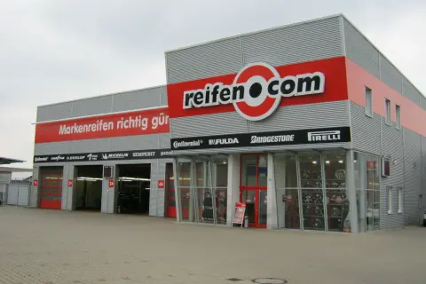 Fassade des reifen.com-Geschäfts mit roten Rolltoren und Reifenregalen im Fenster.