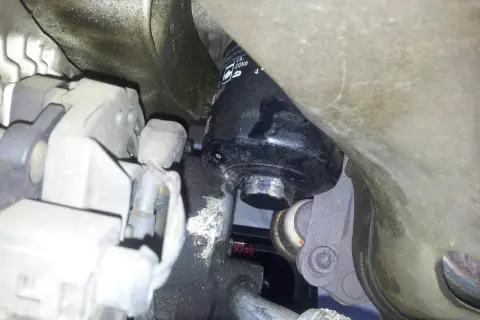 Schwarzer Ölfilter an einem Auto-Motor, umgeben von Metallteilen und Kabeln.