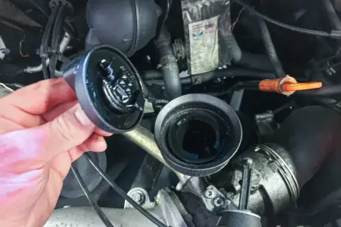 Hand hält abgenommenen Ölfilterdeckel über offenem Ölfiltergehäuse im Motorraum eines VW T5.