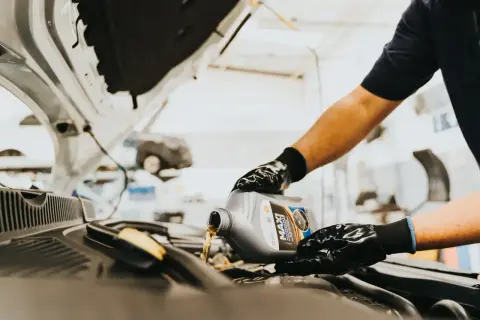 Person mit Handschuhen gießt Motoröl aus einem Kanister in einen Auto-Motor.