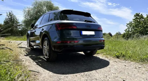 Dunkelgrüner Audi Q5 auf Schotterweg, im Hintergrund grüne Wiesen und Bäume.
