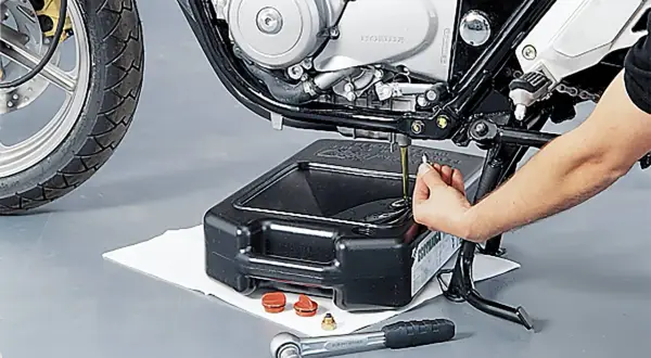 Motorrad-Ölwechsel: Hand leert Öl aus Motor in Auffangwanne. Werkzeug liegt bereit.