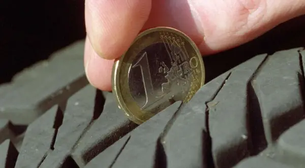 Daumen und 1-Euro-Münze messen Reifenprofiltiefe.