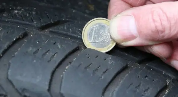 Nahaufnahme eines Reifens, auf dem eine 1-Euro-Münze zur Messung der Profiltiefe liegt.