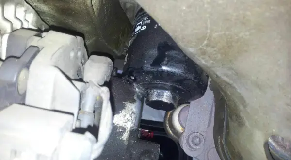 Schwarzer Ölfilter an einem Auto-Motor, umgeben von Metallteilen und Kabeln.