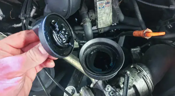 Hand hält abgenommenen Ölfilterdeckel über offenem Ölfiltergehäuse im Motorraum eines VW T5.