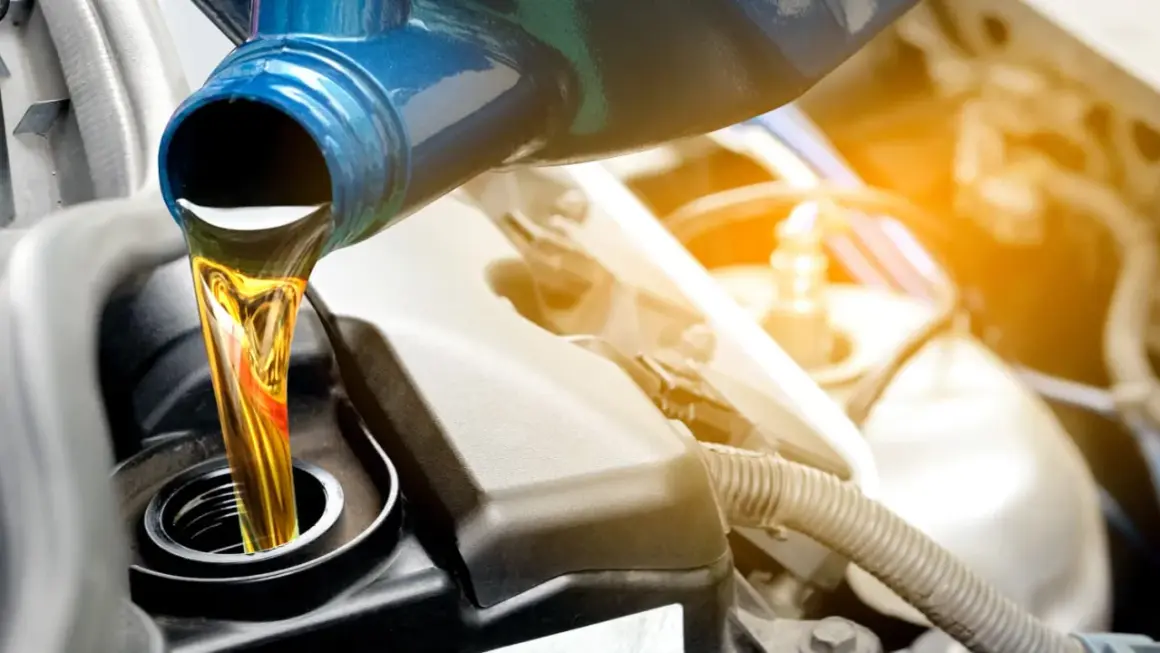 Frisches Öl wird aus einem blauen Behälter in einen Motor gegossen.