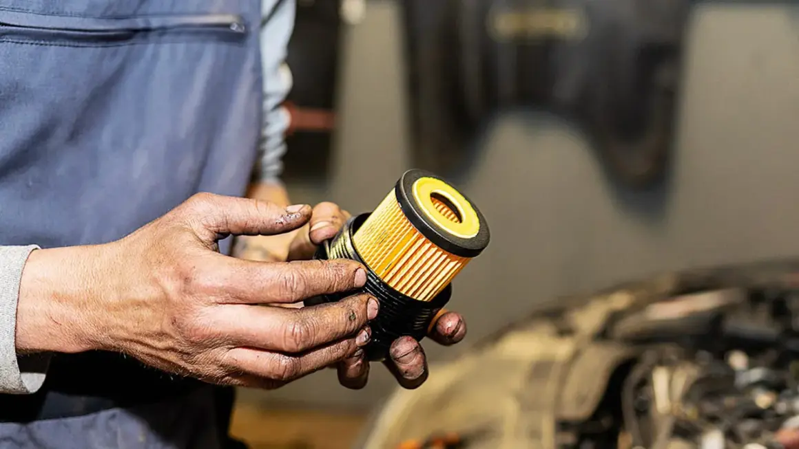 Hände halten einen neuen, gelben Ölfilter für ein Auto.