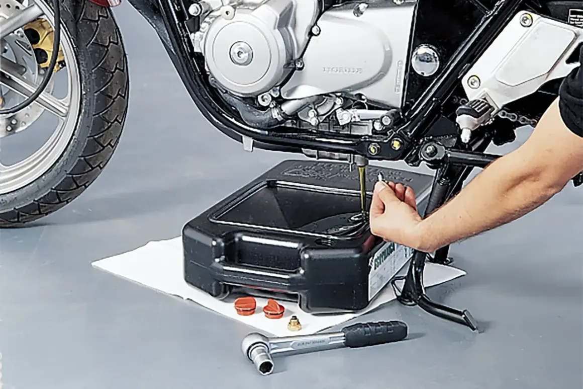 Motorrad-Ölwechsel: Hand leert Öl aus Motor in Auffangwanne. Werkzeug liegt bereit.