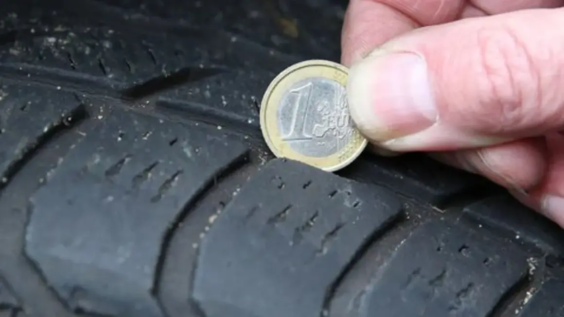 Nahaufnahme eines Reifens, auf dem eine 1-Euro-Münze zur Messung der Profiltiefe liegt.
