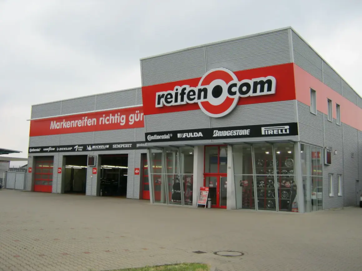 Fassade des reifen.com-Geschäfts mit roten Rolltoren und Reifenregalen im Fenster.