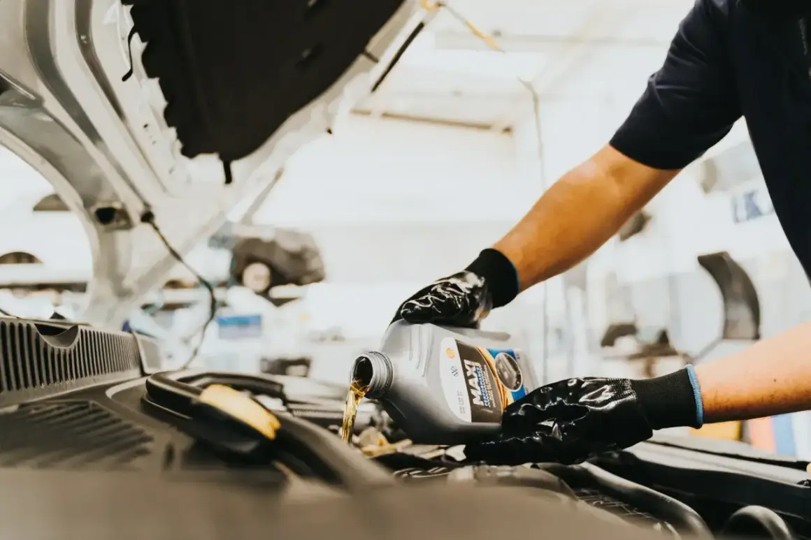 Person mit Handschuhen gießt Motoröl aus einem Kanister in einen Auto-Motor.
