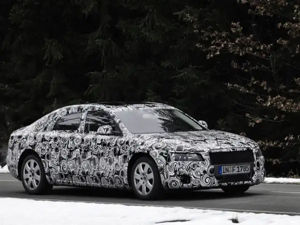 Audi Limousine mit Tarnfolie fährt auf schneebedeckter Straße vor dunklem Wald.