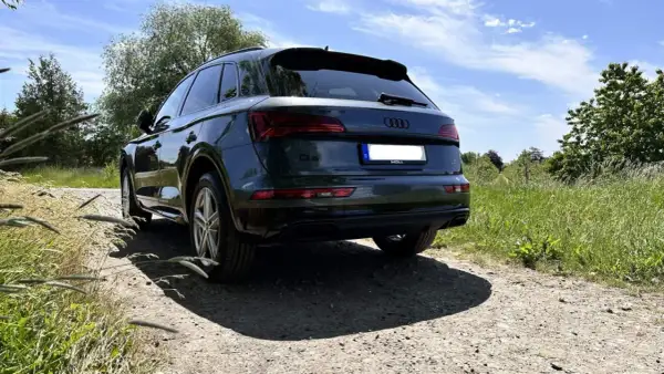 Dunkelgrüner Audi Q5 auf Schotterweg, im Hintergrund grüne Wiesen und Bäume.