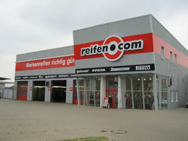 Fassade des reifen.com-Geschäfts mit roten Rolltoren und Reifenregalen im Fenster.